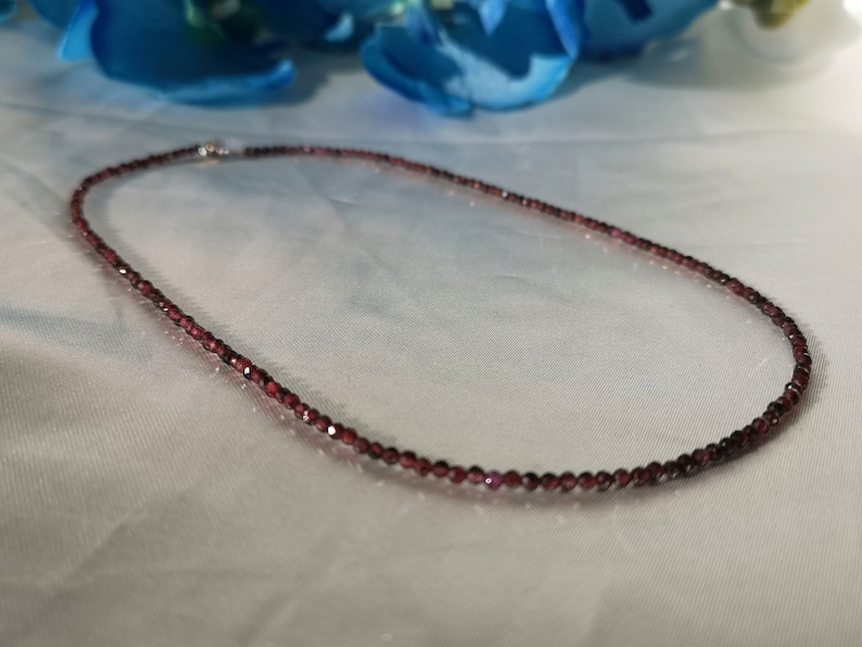 May include: A delicate necklace made of small, dark red garnet beads. The necklace is strung on a silver chain and is approximately 18 inches long.