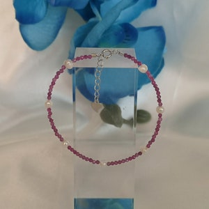 Könnte beinhalten: Ein zartes Armband aus kleinen rosa Perlen und weißen Perlen. Das Armband hat einen silbernen Verschluss.