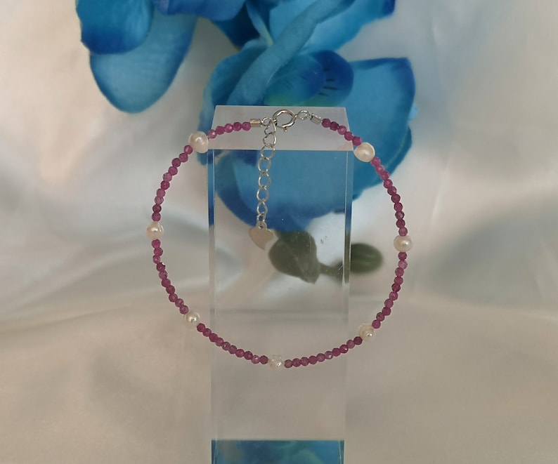 May include: A delicate bracelet made with small pink beads and white pearls. The bracelet has a silver clasp.