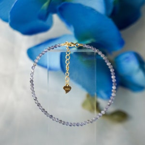 May include: A delicate purple amethyst beaded bracelet with a gold clasp and a small heart charm engraved with "925".