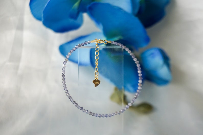 May include: A delicate purple amethyst beaded bracelet with a gold clasp and a small heart charm engraved with "925".