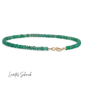 Op de afbeelding: Een delicate armband met kleine, ronde, groene smaragd kralen. De armband is vastgemaakt met een goudkleurige sluiting. De tekst "Lauritas Schmuck" staat in cursief onderaan de afbeelding.
