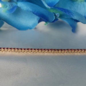 May include: A gold chain bracelet with small, red gemstones set in a row.