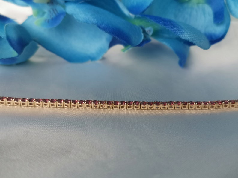 May include: A gold chain bracelet with small, red gemstones set in a row.