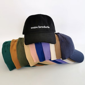 May include: A stack of 10 blank baseball caps in various colours, including green, brown, beige, pink, blue, purple, and white. The top cap is black with the text "votre broderie" embroidered in white.