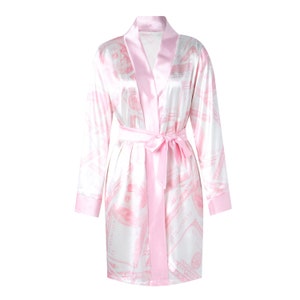 May include: A pink satin robe with a white background and a pink dollar bill print. The robe has a matching pink sash.