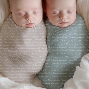 Peut inclure: Deux nouveau-nés emmaillotés dans un tissu doux et à motifs. Le tissu présente un motif d'écriture manuscrite délicate en gris clair. Les bébés dorment paisiblement, côte à côte.