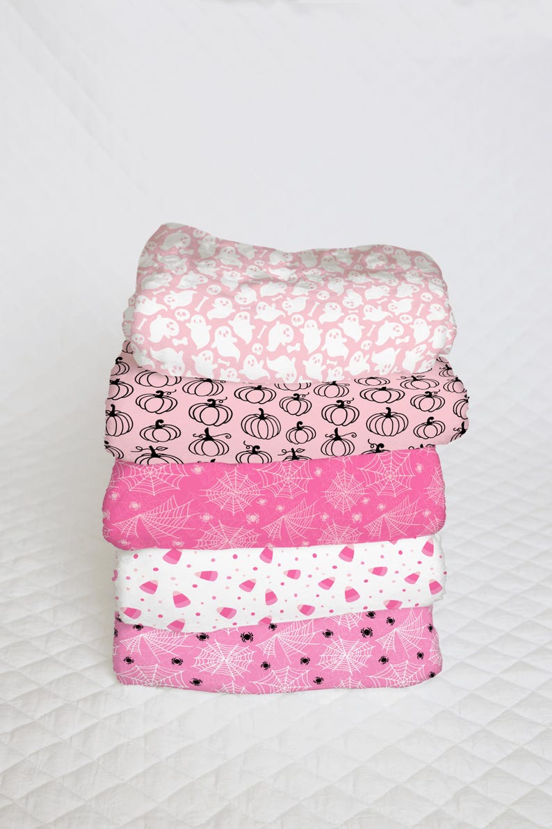 May include: A stack of five pink fabric squares with different Halloween-themed patterns. The patterns include ghosts, pumpkins, spiderwebs, and candy corn.