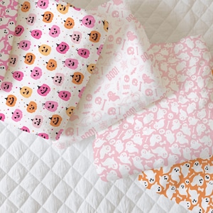 K&ouml;nnte beinhalten: Vier verschiedene Stoffmuster mit Halloween-Motiven. Die Muster umfassen rosa Geister, orangefarbene K&uuml;rbisse und die Worte "Boo!" in rosa. Die Stoffe sind alle wei&szlig; mit rosa und orangefarbenen Akzenten.