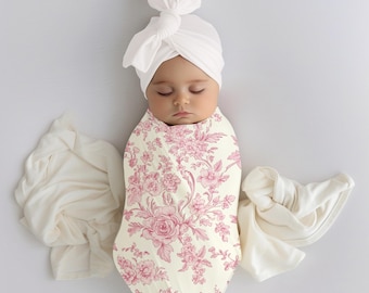 Könnte beinhalten: Ein Baby, das in ein weißes und rosafarbenes Blumenmuster gewickelt ist. Das Baby trägt einen weißen Turban.