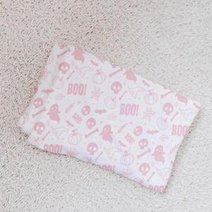 May include: A white fabric with a pink Halloween print featuring ghosts, pumpkins, skulls, bats, witch hats, and the word "BOO!" repeated throughout.