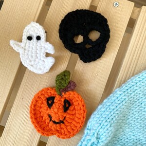 May include: Three crocheted Halloween decorations: a white ghost, a black skull, and an orange pumpkin with a black smiling face.