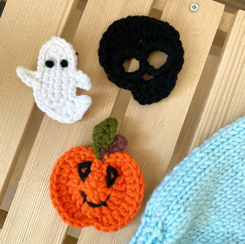 May include: Three crocheted Halloween decorations: a white ghost, a black skull, and an orange pumpkin with a black smiling face.