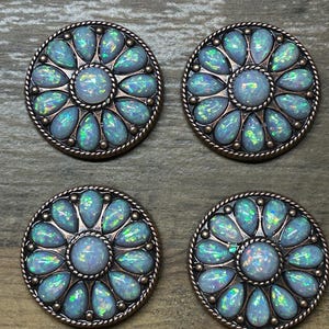 May include: Four round, copper-toned metal buttons with a floral design. Each button features a central opal-like stone surrounded by smaller opal-like stones in a flower shape.
