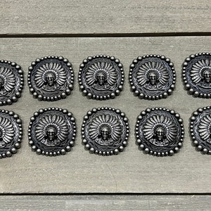 May include: Ten silver-toned metal buttons with an embossed design of a Native American chief wearing a headdress. The buttons are round and have a beaded edge.