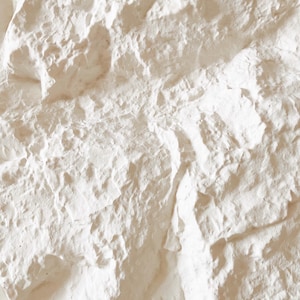 May include: Close-up of a textured, off-white wall surface. The surface has a rough, uneven texture with visible ridges and crevices, creating a natural, organic appearance. The color is a warm, neutral tone, suitable for various interior design styles.