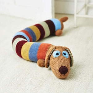 May include: A knitted dachshund dog doorstop with a striped body and brown head. The dog has blue eyes and a brown nose.
