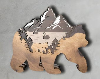 May include: A wooden bear silhouette with a layered mountain scene inside. The mountain scene features a lake with swans and trees. The bear is brown and the mountain scene is gray and white.