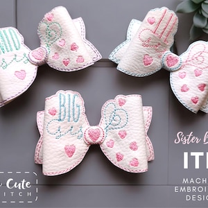 May include: White embroidered hair bows with pink and teal stitching. The bows have the words "MID SIS" and "BIG SIS" embroidered on them, along with heart designs. The text "Sister Bows ITH Machine Embroidery Design" is also visible.