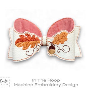 May include: A white bow with a pink interior and orange leaf and acorn embroidery. The bow has a stitched design with the text "In The Hoop Machine Embroidery Design".