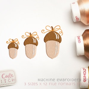 May include: Three acorn embroidery designs in different sizes. The acorns are brown with a light brown cap and a light brown stem. The acorns are decorated with a yellow bow. The designs are perfect for fall crafts and decorations.