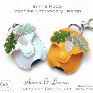 May include: Two hand sanitizer holders in the shape of acorns with leaves. One is white, the other is yellow. Both have a metal clasp and a button closure. The text "Acorn & Leaves hand sanitizer holder" is below the holders.