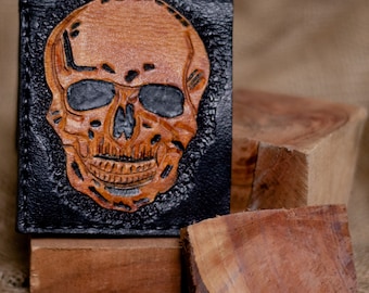 May include: A black leather wallet with a tooled skull design. The skull is brown and has black eyes.