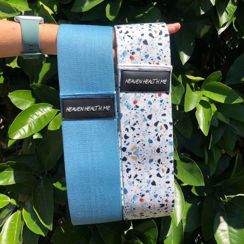 May include: Two resistance bands, one blue and one white with a blue, black, and orange terrazzo pattern. Both bands have a black label that reads "Heaven Health Me."