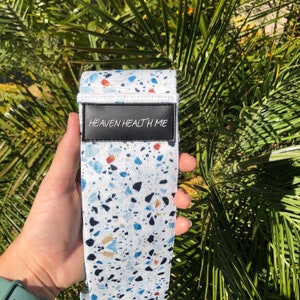 May include: White exercise band with a blue, black, and orange terrazzo pattern. The band has a black label with the text "HEAVEN HEALTH ME" printed in white.