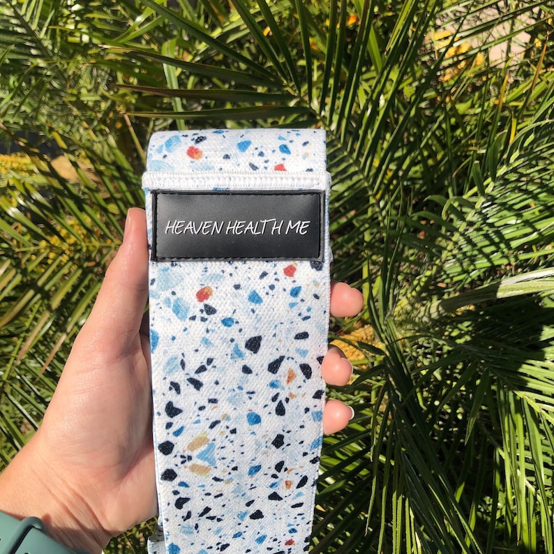 May include: White exercise band with a blue, black, and orange terrazzo pattern. The band has a black label with the text "HEAVEN HEALTH ME" printed in white.