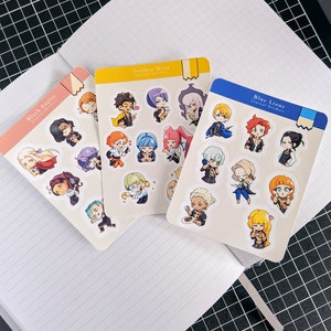 May include: Four sets of colorful journal stickers featuring characters from the Fire Emblem: Three Houses video game. Each set is labeled with the house name: Black Eagles, Golden Deer, Blue Lions, and a fourth set with no house name. The stickers are printed on white cardstock.