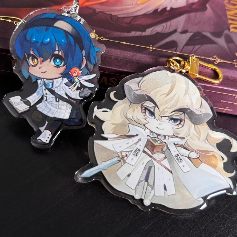 K&ouml;nnte beinhalten: Zwei Schl&uuml;sselanh&auml;nger mit Anime-Charakteren. Der erste Schl&uuml;sselanh&auml;nger zeigt ein blahaariges M&auml;dchen in einem wei&szlig;en und blauen Outfit, das ein Buch h&auml;lt. Der zweite Schl&uuml;sselanh&auml;nger zeigt ein wei&szlig;haariges M&auml;dchen in einem wei&szlig;en Outfit, das ein Schwert h&auml;lt. Beide Schl&uuml;sselanh&auml;nger sind aus klarem Acryl.