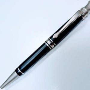 May include: A black and silver pen with a sleek design. The pen features a silver clip and accents, with a black barrel. The pen's tip and top are also silver. The pen is a writing instrument.
