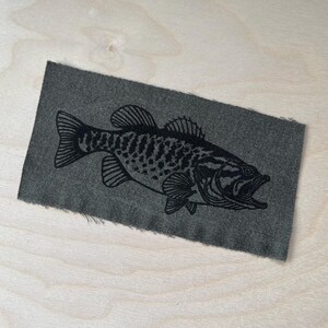Könnte beinhalten: Eine Schwarzweißillustration eines Barsches auf einem dunkelgrauen Stoffstück.