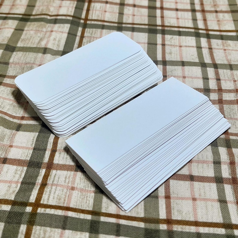 Puede incluir: Dos montones de tarjetas rectangulares blancas en blanco con esquinas redondeadas. Las tarjetas est&aacute;n cuidadosamente apiladas, mostrando los bordes de cada tarjeta. El fondo es un patr&oacute;n de cuadros marr&oacute;n y beige.