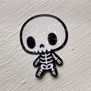 May include: A black and white sticker of a cartoon skeleton with a sparkly skull. The skeleton is wearing a black and white skeleton costume with a sparkly design.