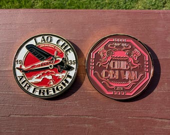 May include: Two round, metallic coins. One coin features a red and white airplane design with the text "LAO CHE AIR FREIGHT 1935". The other coin has a red design with the text "CLUB OBI WAN CHINA".
