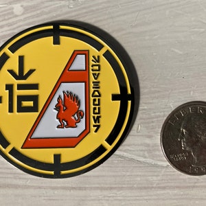 May include: A yellow and black circular pin with a red and white ship design. The ship has a red griffin on the side and the text "SEEDSHIP 7" on the side. The pin also has a black arrow pointing down and the number "16" on the left side.