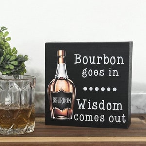 May include: Black wooden sign with a white graphic of a bottle of bourbon and the text "Bourbon goes in... Wisdom comes out".