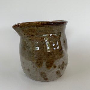 May include: A brown and white ceramic pitcher with a speckled glaze. The pitcher has a rounded body and a wide, slightly flared lip.