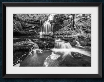 May include: A black and white photograph of a waterfall cascading over rocks in a forest. The water is flowing smoothly and the rocks are covered in moss.