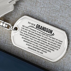 May include: A silver-colored dog tag with the text "TO OUR GRANDSON" and a heartfelt message. The tag is attached to a metal chain. The text is in a clear, easy-to-read font.