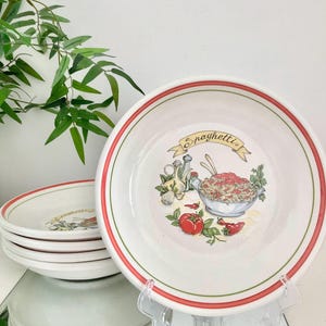 May include: White ceramic spaghetti bowls with a red and green rim. Each bowl features a spaghetti illustration with the word "Spaghetti" on a banner. A stack of bowls is visible.