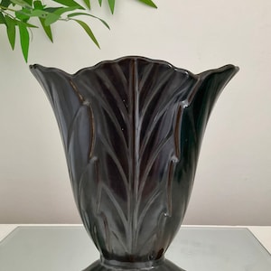 May include: A black ceramic vase with a fluted design. The vase has a wide mouth and a narrow base.