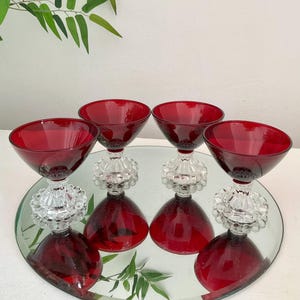 May include: Set of four red glass stemmed dessert cups with clear, beaded bases. The cups are arranged on a mirrored surface.