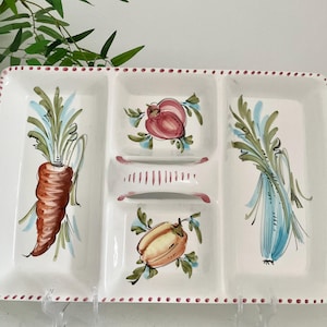 May include: A rectangular white ceramic serving tray with three divided sections. The tray features hand-painted illustrations of a carrot, a pomegranate, a bell pepper, and a leek. The outer rim is decorated with a pattern of small pink dots.