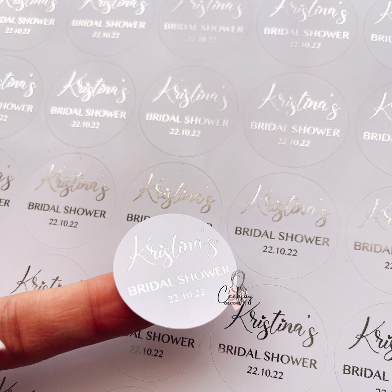 以下が含まれることがあります： 「Kristina's Bridal Shower 22.10.22」と銀色の箔押し文字が書かれた白い丸いステッカーです。