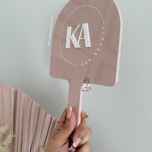 Puede incluir: Un letrero rosa p&aacute;lido con un asa, que muestra el texto blanco "KA" dentro de un c&iacute;rculo, con las palabras "KAYLI ANN BEAUTY" que lo rodean. El letrero lo sostiene una persona. El letrero tambi&eacute;n tiene el texto "ceehjoycreations.com.au".