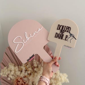 Puede incluir: Dos paletas rosas para arte de tatuaje cosm&eacute;tico. Una paleta tiene el nombre "Sibina" en escritura blanca y el texto "Cosmetic Tattoo Art". La otra paleta tiene el texto "Dolled by Dani.E" y una ilustraci&oacute;n de un pincel de maquillaje. Ambas tienen un mango.