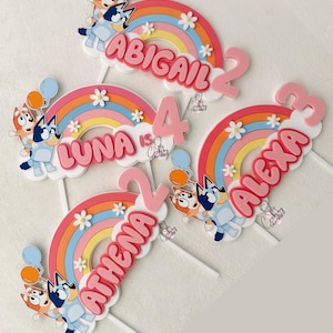 Pu&ograve; includere: Quattro topper per torta a forma di arcobaleno colorati con i nomi Abigail, Luna, Athena e Alexa, ognuno con un numero e un cane dei cartoni animati.
